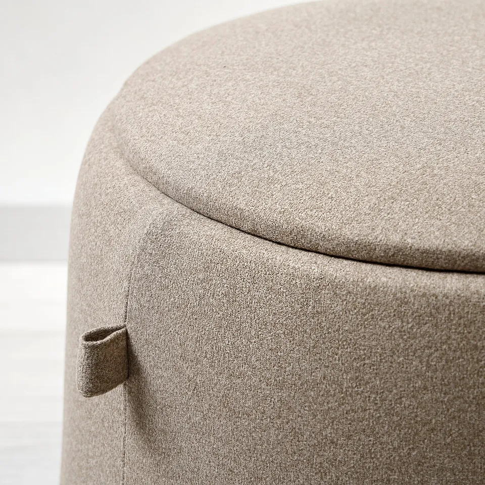 Round upholstered stool with smooth, beige fabric and tufted detail on the front.