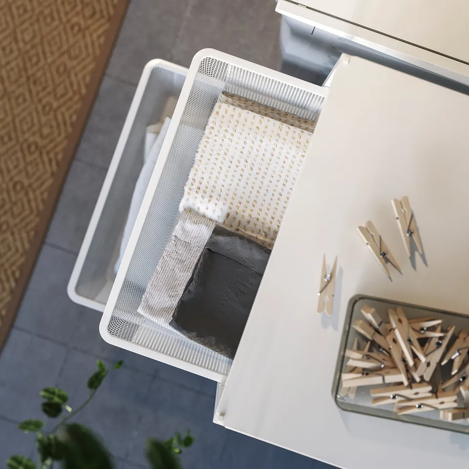 White JONAXEL storage box with cloth inside, wooden clothespins on table, wicker chair.