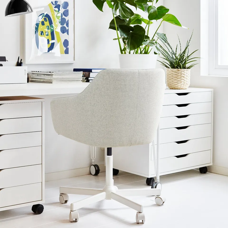 Modern white home office setup. TOSSBERG chair matches white drawers. Potted plants decorate, abstract art on wall.