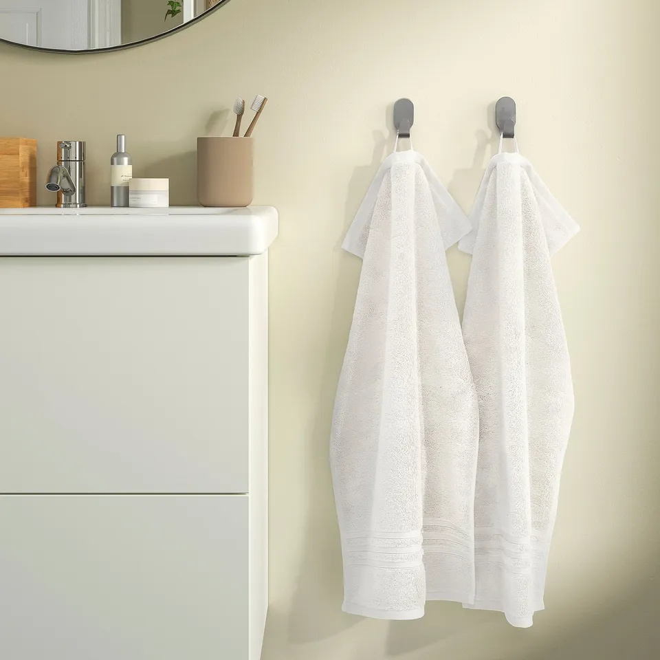 Two white towels hang on hooks beside a white vanity with a beige countertop.