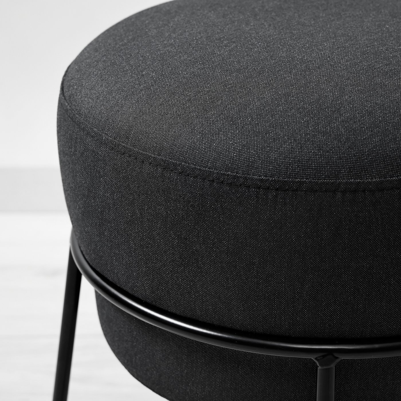 Modern round footstool with sleek black metal frame and plush, dark grey fabric cover, offering comfort and contemporary style.