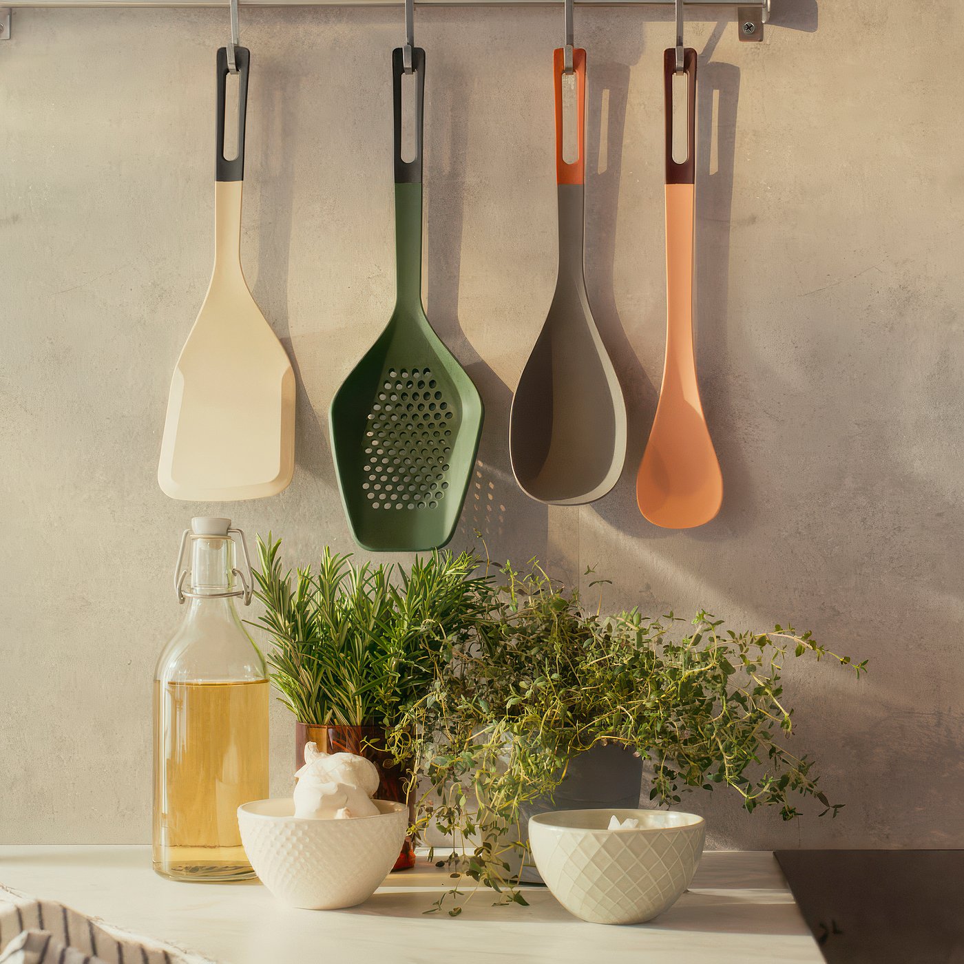 Four colourful cooking utensils hang neatly, perfect for stirring and mixing; a glass bottle and white bowls with herbs sit on the counter.