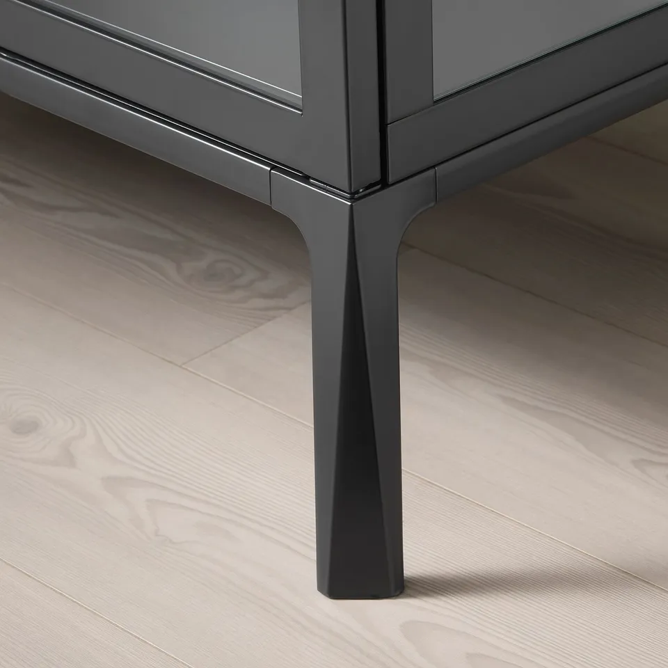 Modern cabinet with sleek black metal leg, glossy finish, and glass panels on wooden floor.