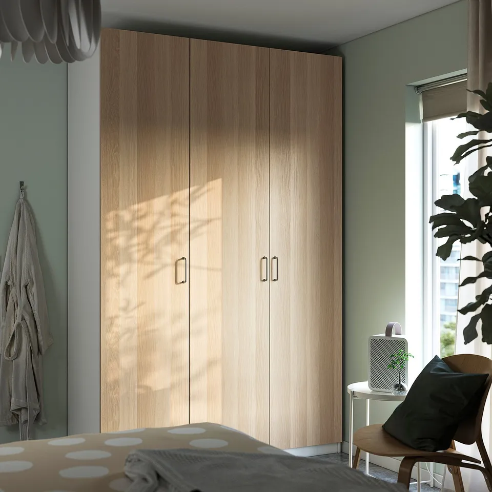 Modern bedroom large light wood PAX wardrobe, tall plant, cosy brown chair, and polka dot bedding.