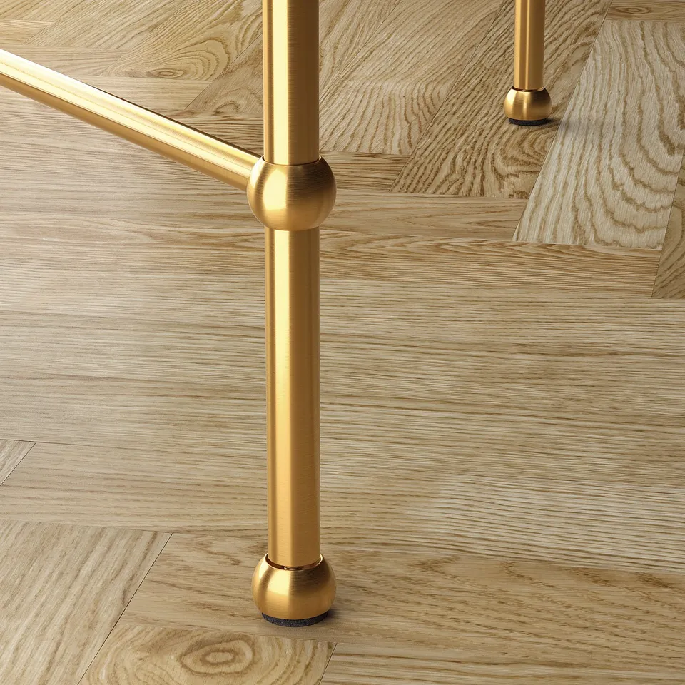 Elegant gold metal table leg with scrolling base, adjustable foot on polished wooden floor.