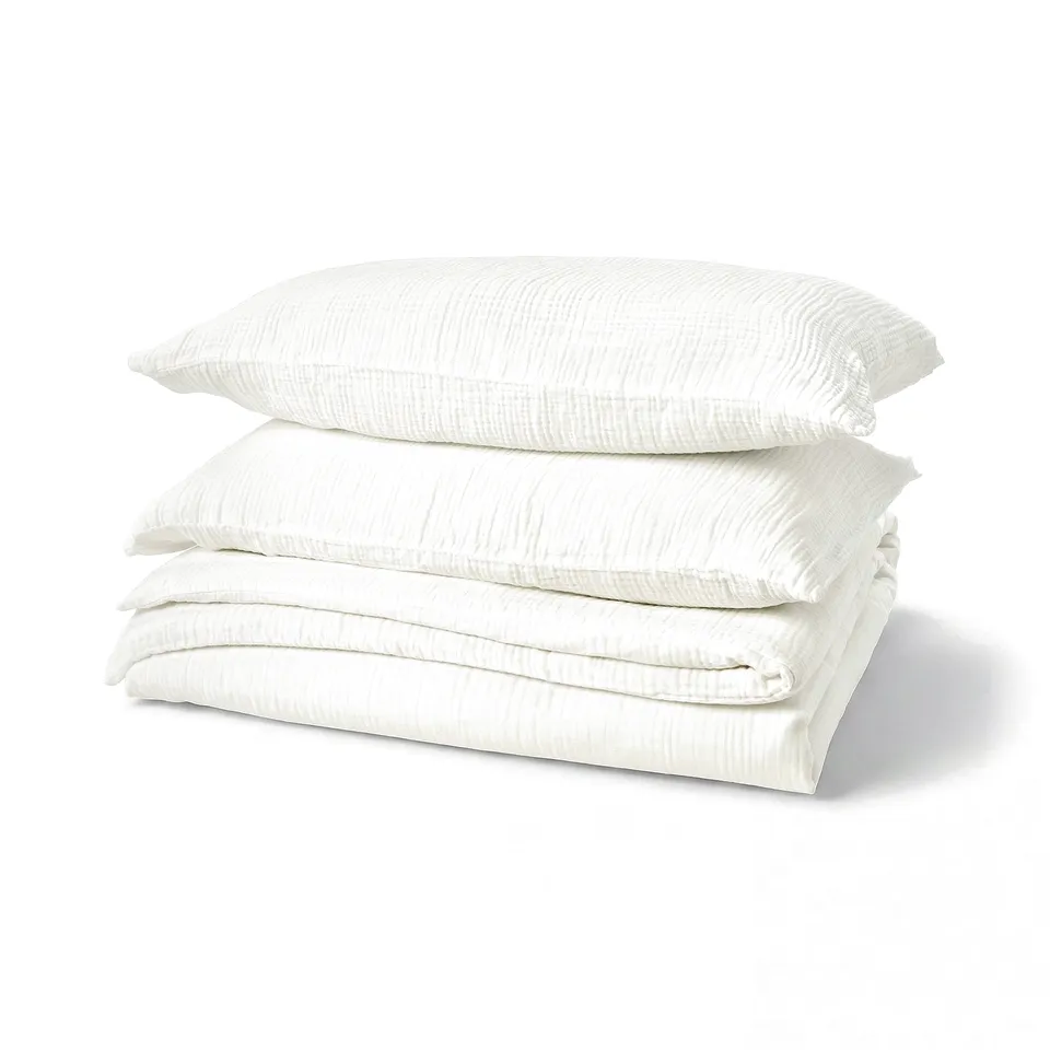 Stack of white, organic cotton bedding, including duvet cover and pillowcases, neat and folded, feature soft, wavy texture.