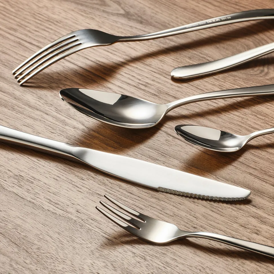 Stainless cutlery on wooden table, reflecting light.