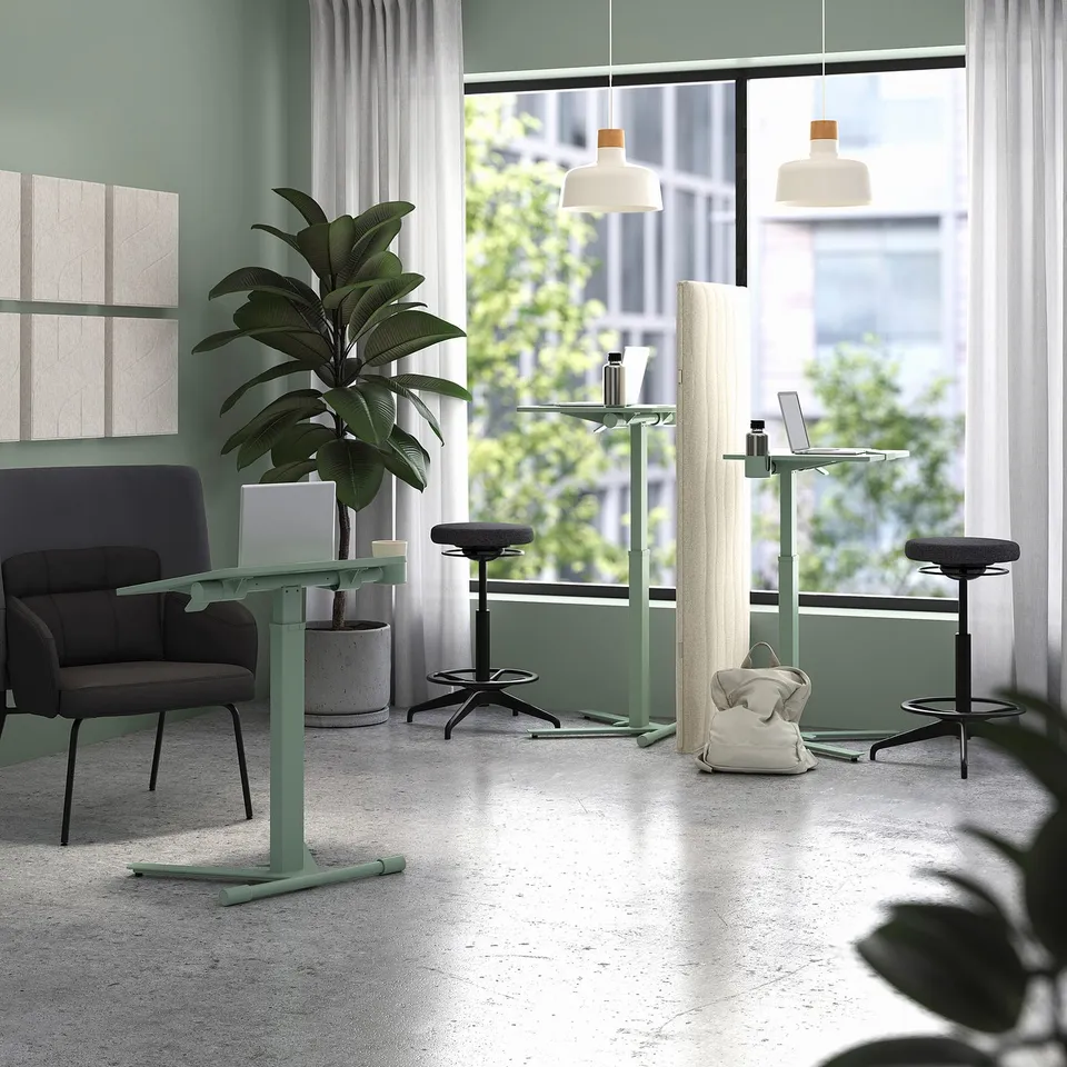 Modern office with acoustic screens, black chairs, green tables, city view, and plant.