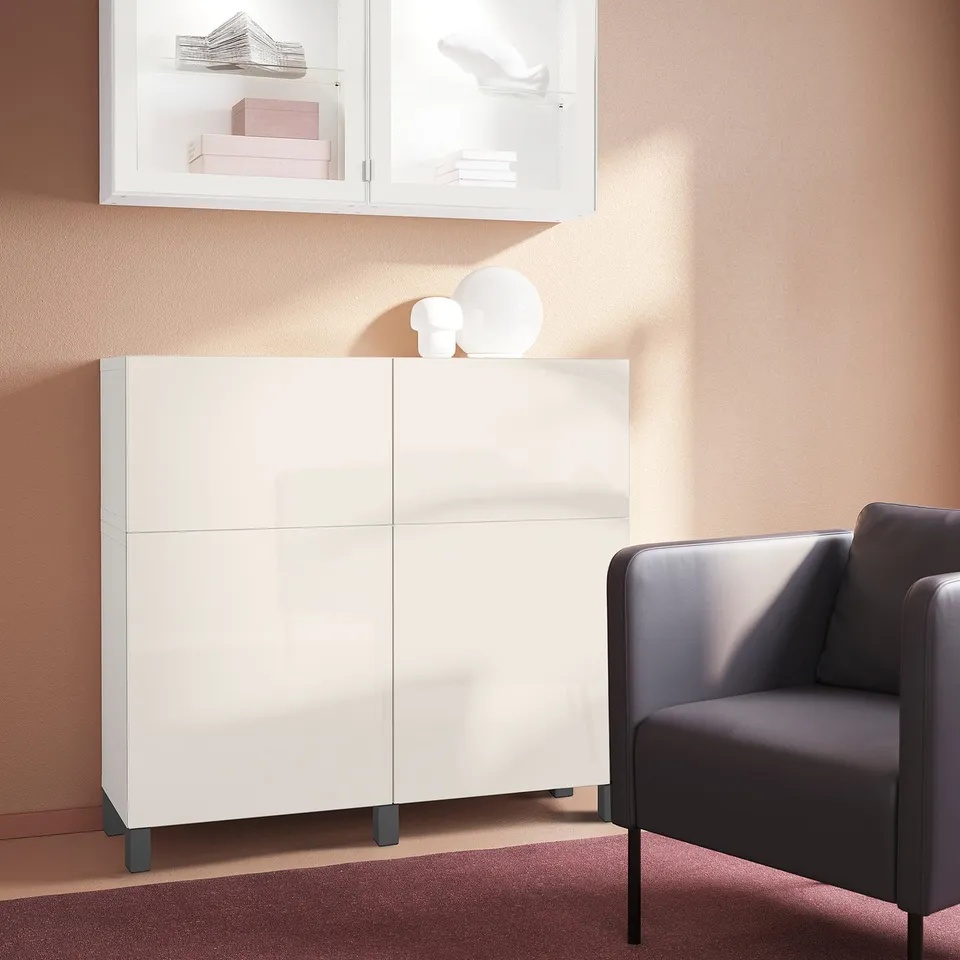 STUBBARP storage unit with dark grey wood legs, next to armchair on rug. Glass cabinet tops holding decorative items.