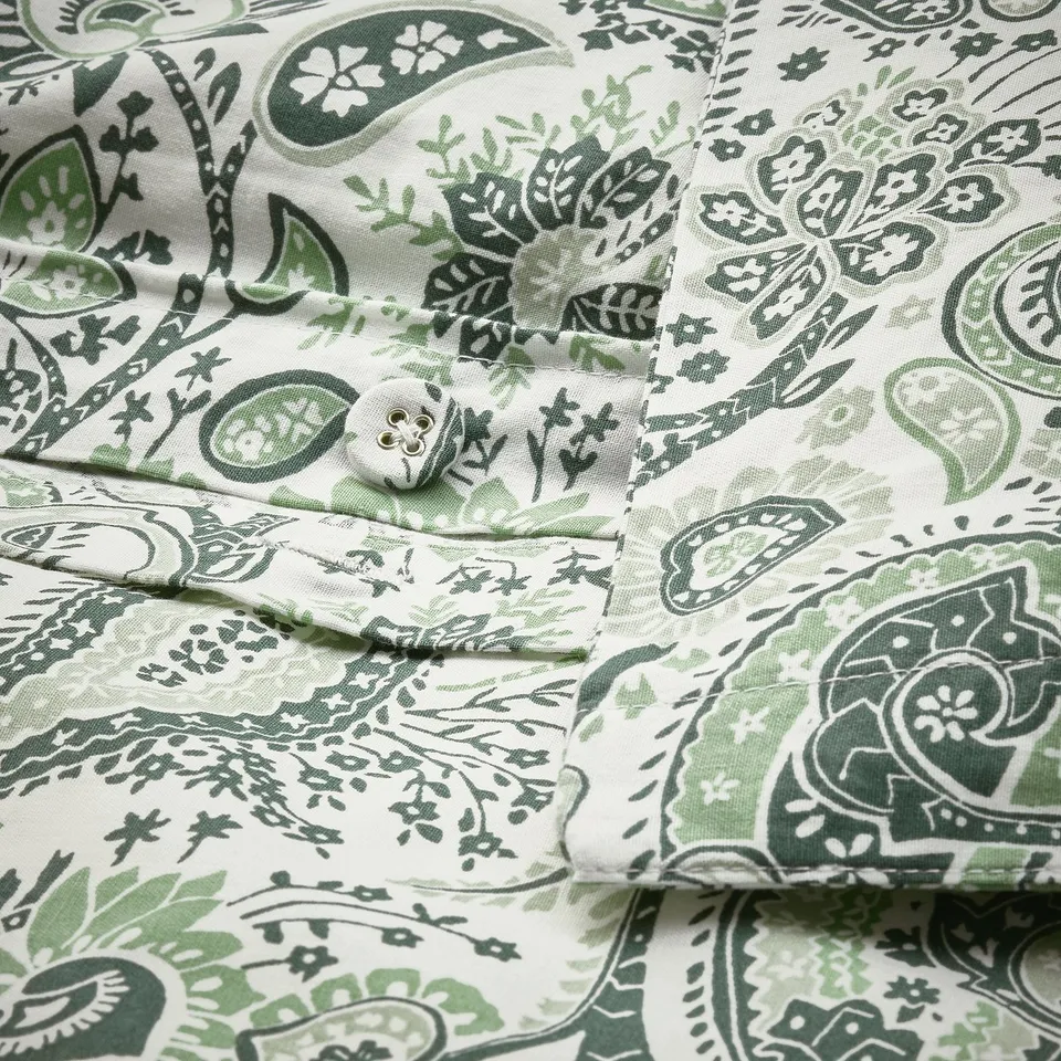Green and white paisley-patterned pillowcase with fabric-covered buttons for closure.