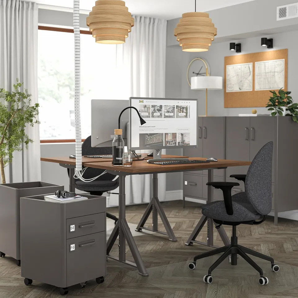 IDÅSEN desk setup with large monitor, laptop, chair, and file cabinet. Two pendants above.