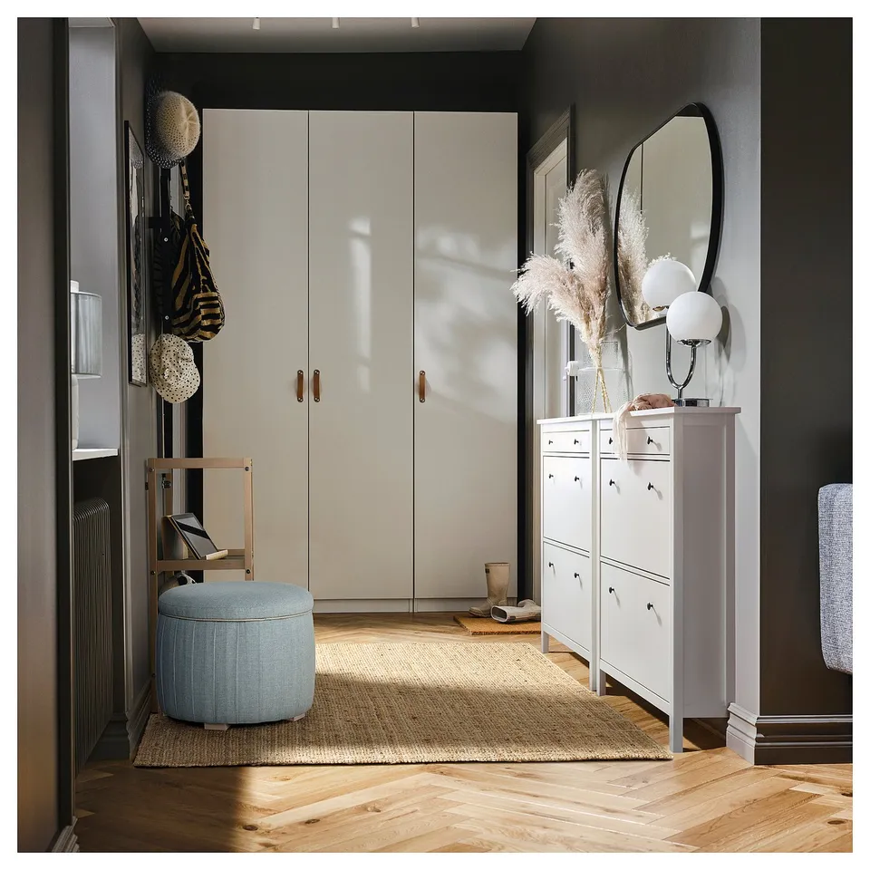 A modern, stylish entryway with a light-colored wardrobe, a storage unit, and a light blue, cylindrical storage ottoman on a jute rug.