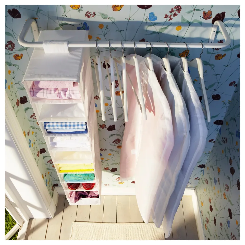 Closet with MULIG rack holding clothes, featuring floral wallpaper, white hangers, and clear storage boxes with various coloured fabrics.