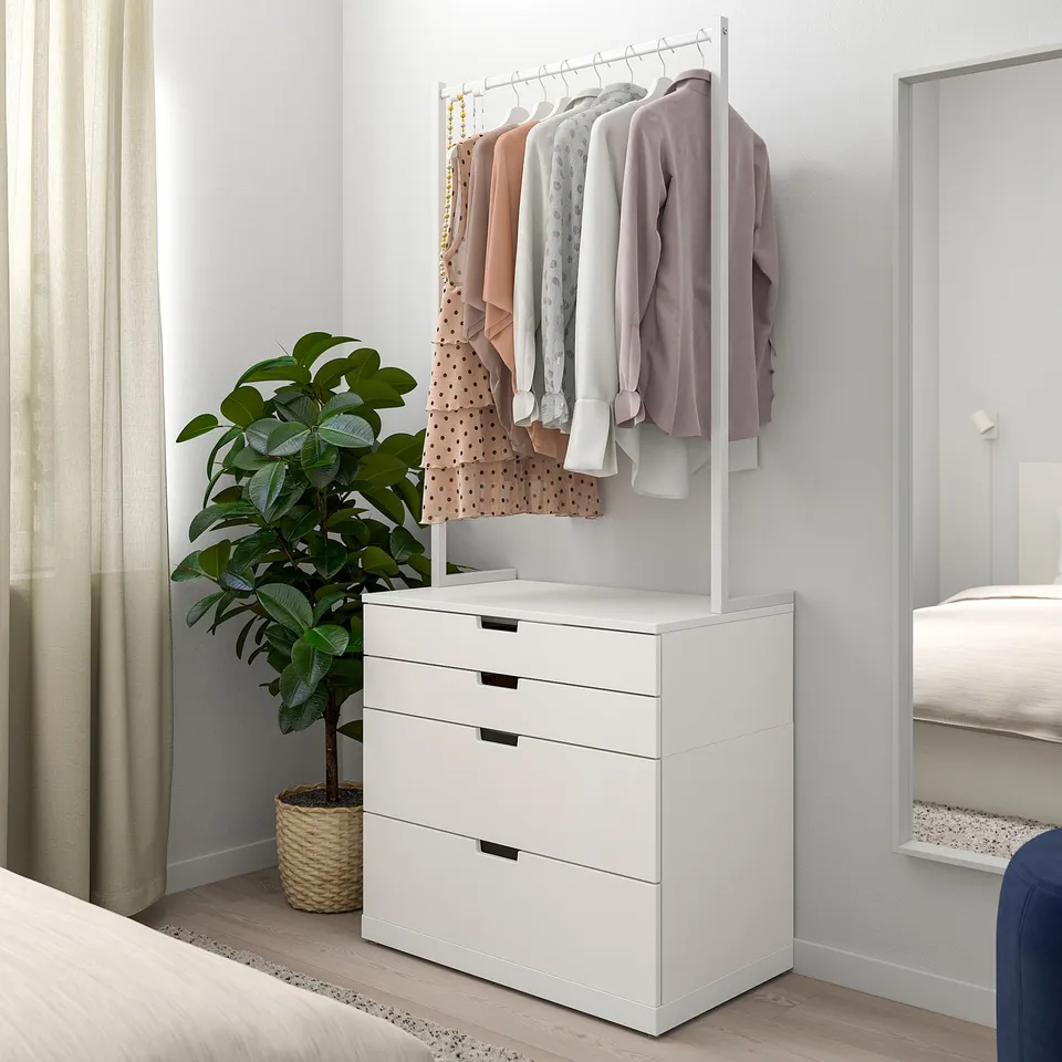 Minimalist white NORDLI chest drawers under clothes rail, beside tall plant, near bed in serene room.