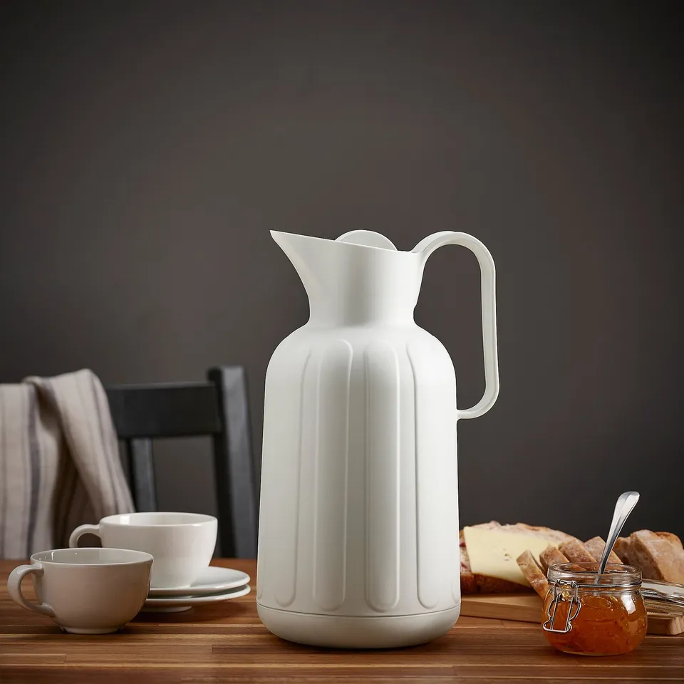 Vacuum flask on table with cups, bread, and jam.