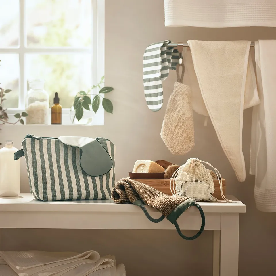Bathroom scene with blue-striped bag, green hair towel, and white towels hanging.