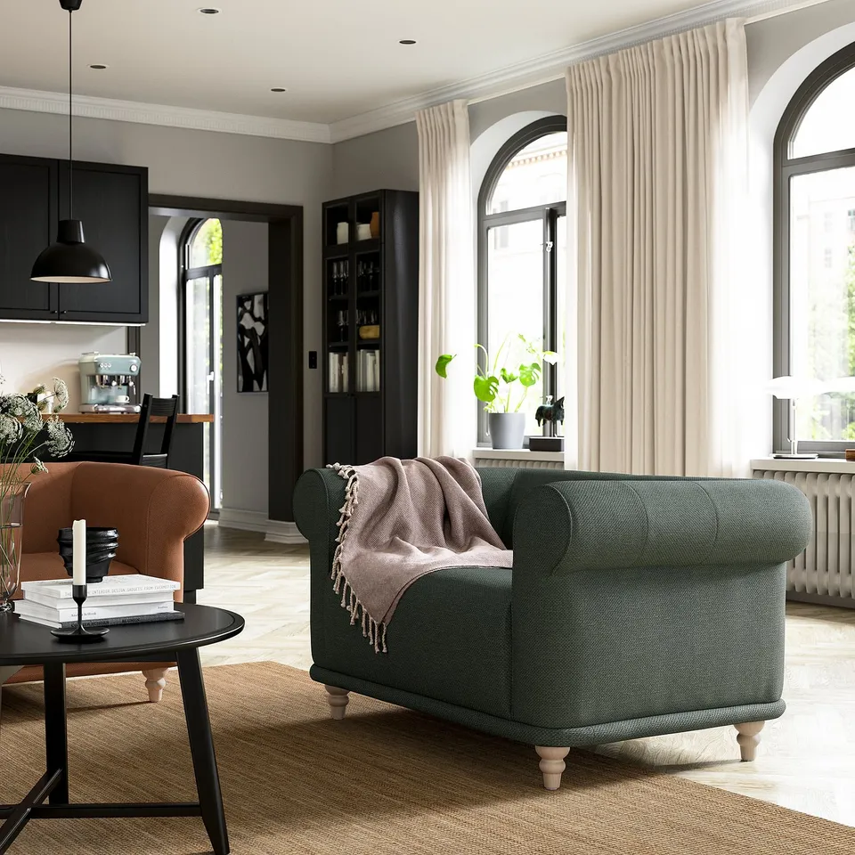 Modern living room with green VISKAFORS armchair, brown side table, books, and large windows with curtains. Cosy, inviting decor.