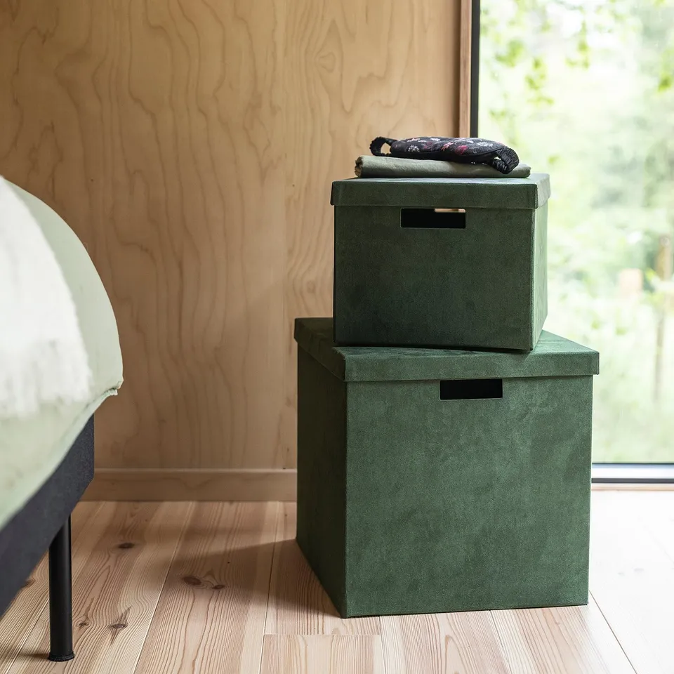 Two green GJÄTTA storage boxes stacked with blankets next to bed, perfect for kallax shelves.