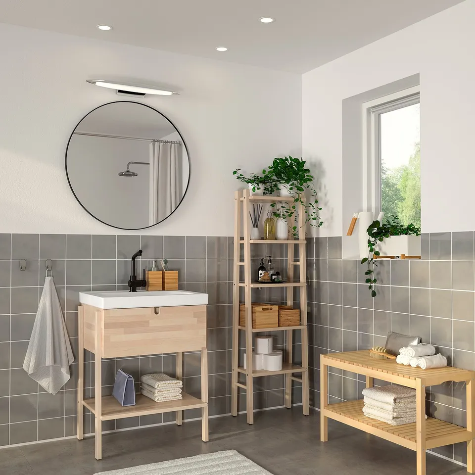 Modern bathroom with black round mirror above wooden vanity, reflecting greenery for a bright, elegant look.