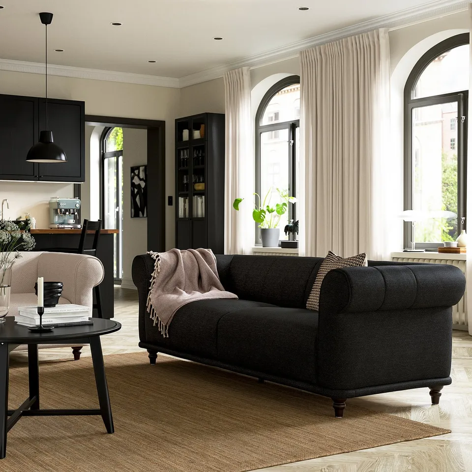 Modern living room with VISKAFORS black sofa, light pink chair, wooden floor, large arched windows, and black furniture.