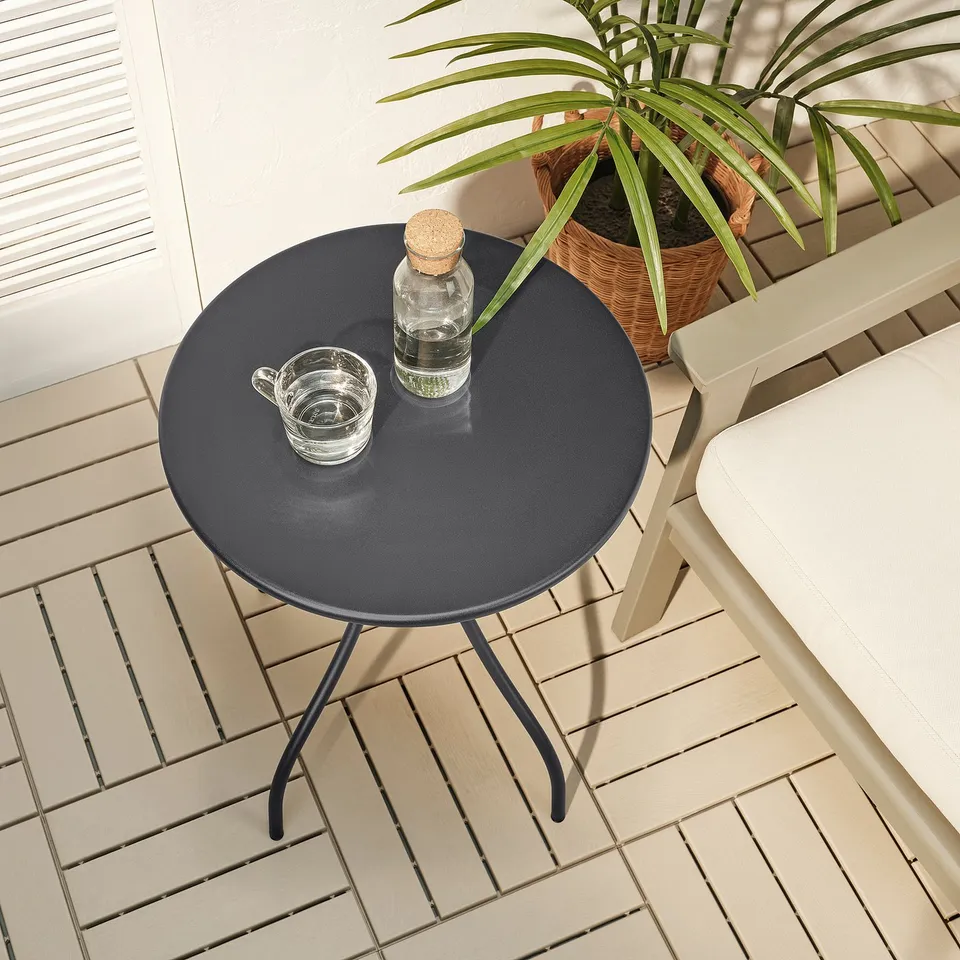 Small round outdoor table with a bottle and cup on it, beside a chair.