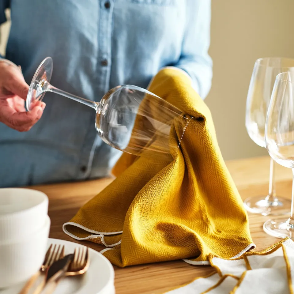 Person holding wine glass with yellow napkin and dishes on wooden table.