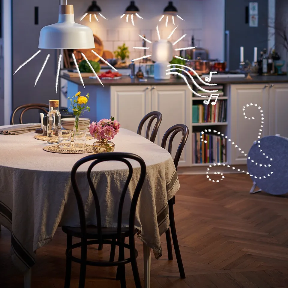 Modern kitchen table with grey cloth, black chairs, and flowers. Smart-controlled pendant lamp.
