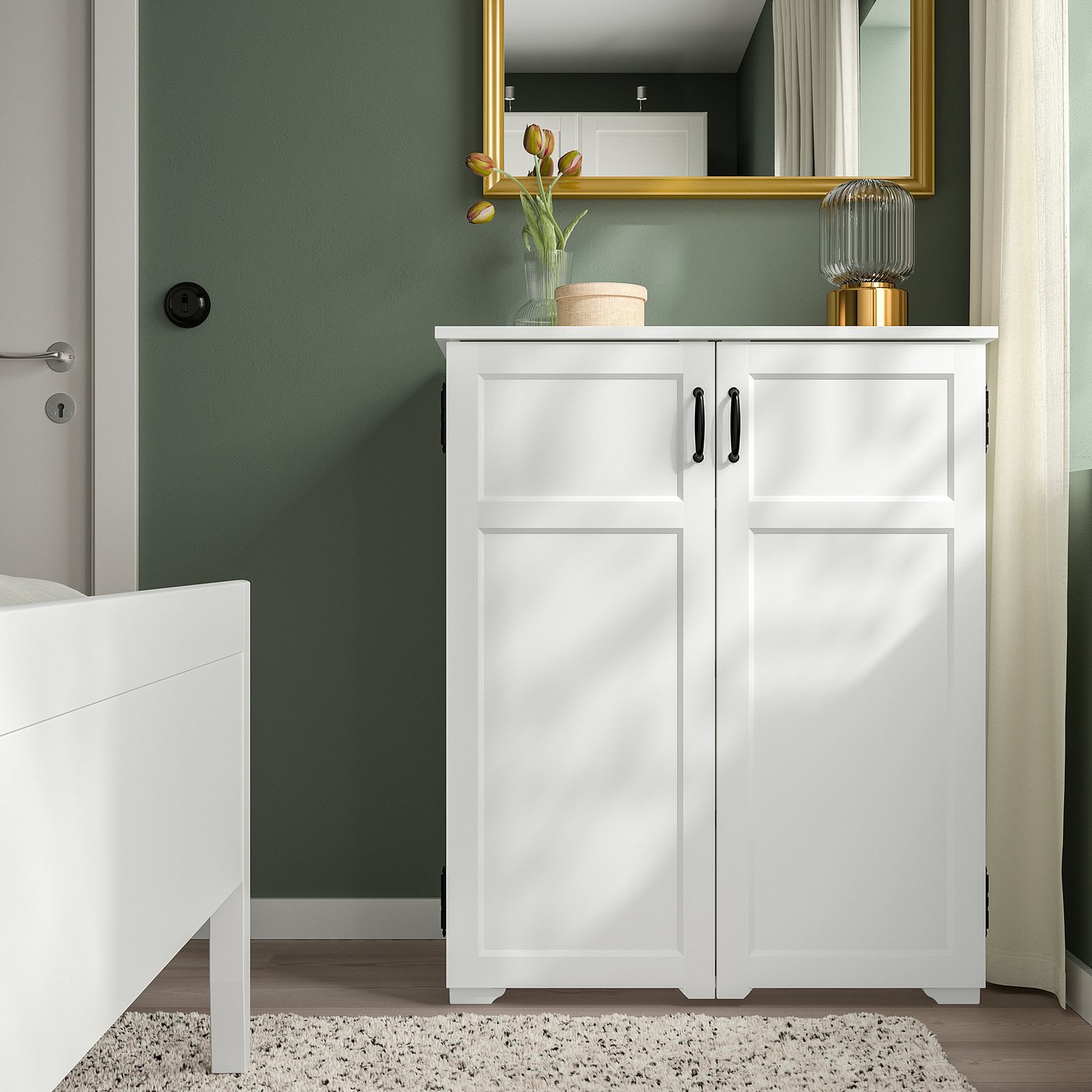 White GREÅKER cabinet with 2 doors, green wall, knitted rug, bed frame, mirror, decor.