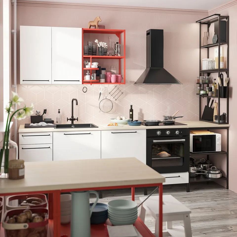 Modern kitchen with red and black accents, featuring a white countertop, built-in oven, sink, and various appliances on wooden floor.