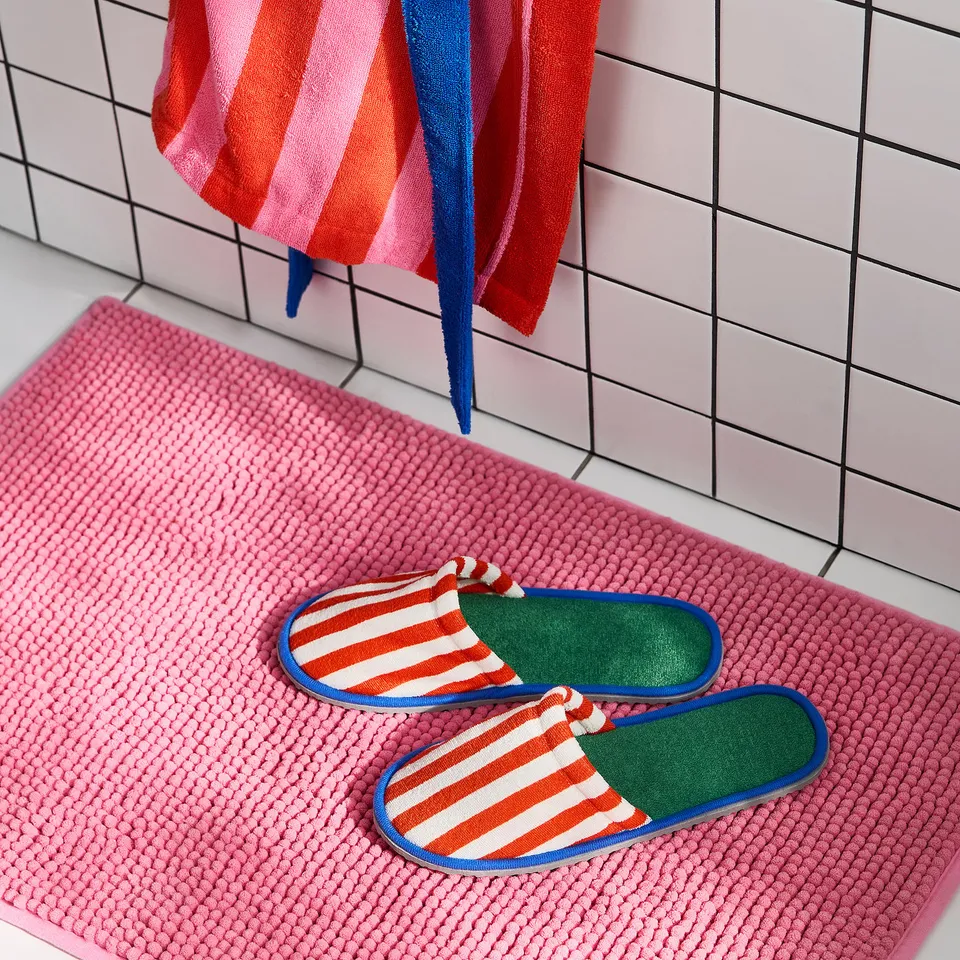 Orange-and-white striped slippers on pink rug in bathroom.