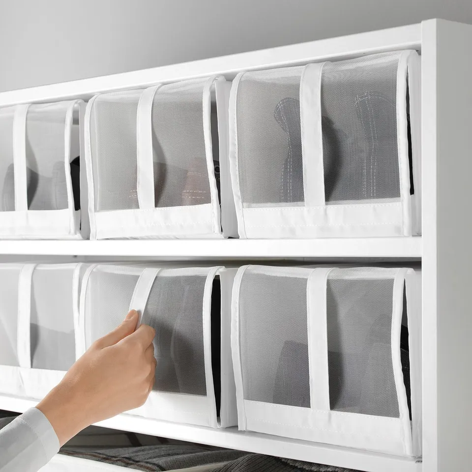 Hand reaches for a mesh SKUBB shoe box, one of four fitting side by side in a 100 cm wardrobe. Mesh allows air circulation and easy visibility.