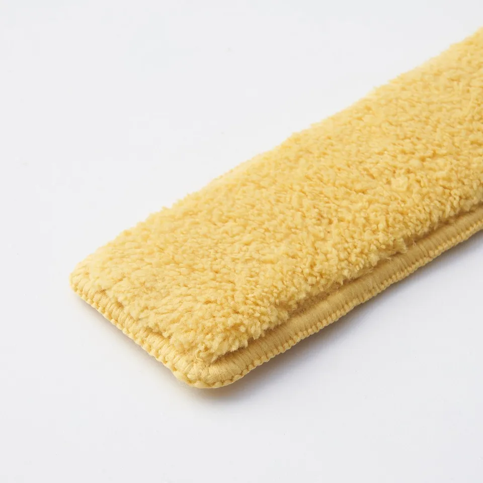 Folded yellow cleaning pad, soft textured surface, stitched edges, laid on white background.