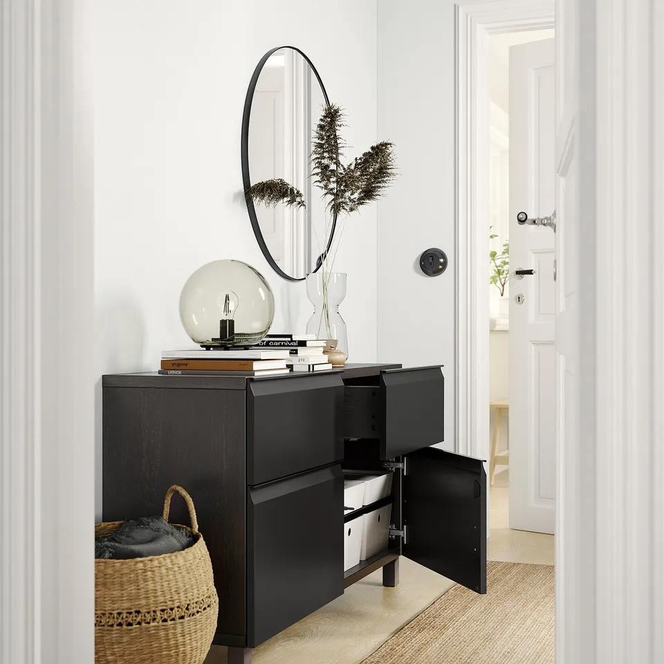 Black BESTÅ sideboard with open doors, displaying shelves, beneath a circular mirror. Topped with a globe light, books, and a vase.
