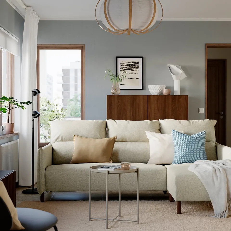 Cosy living room with MANNARP sofa, blue/beige cushions, side table, cabinet, lamp, and large windows.