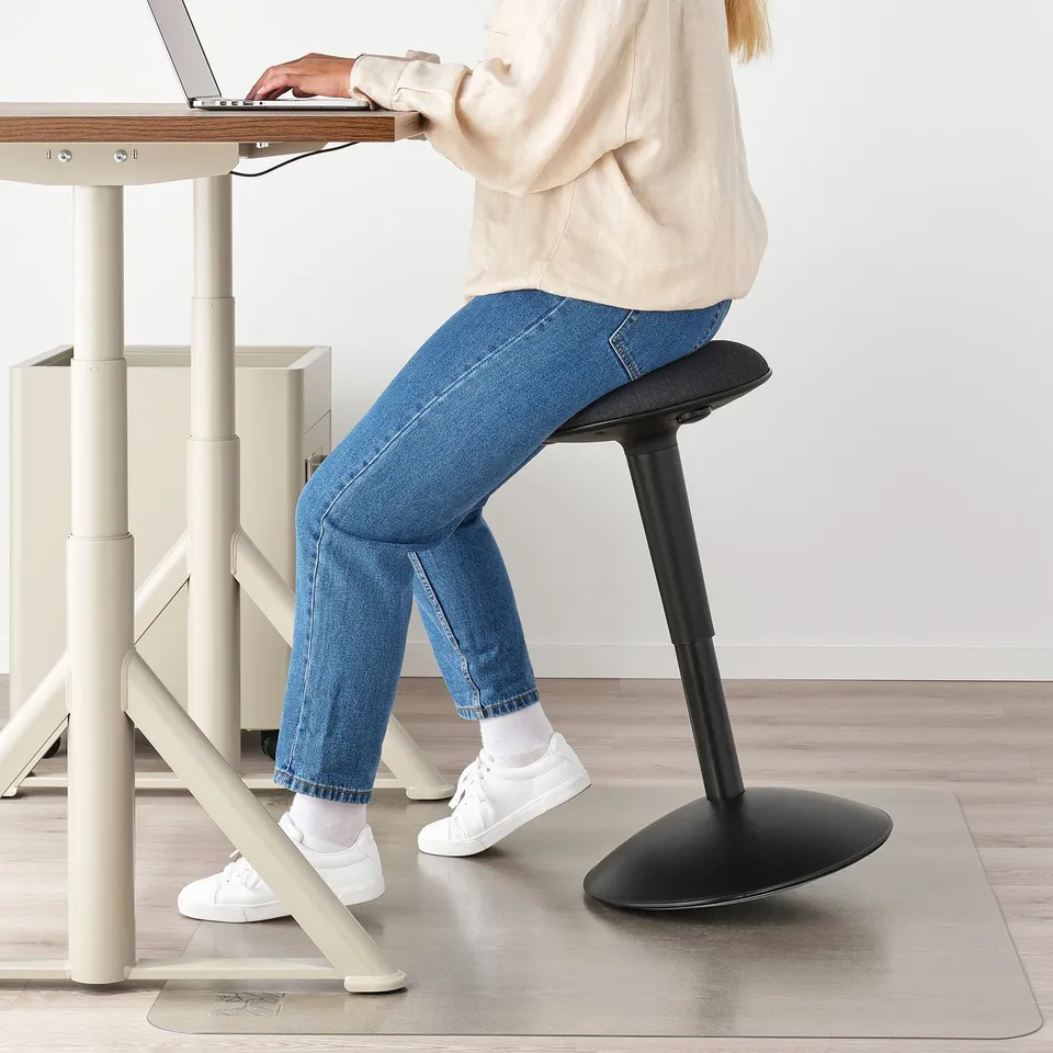 Person using NILSERIK active sitting support at standing desk with laptop.