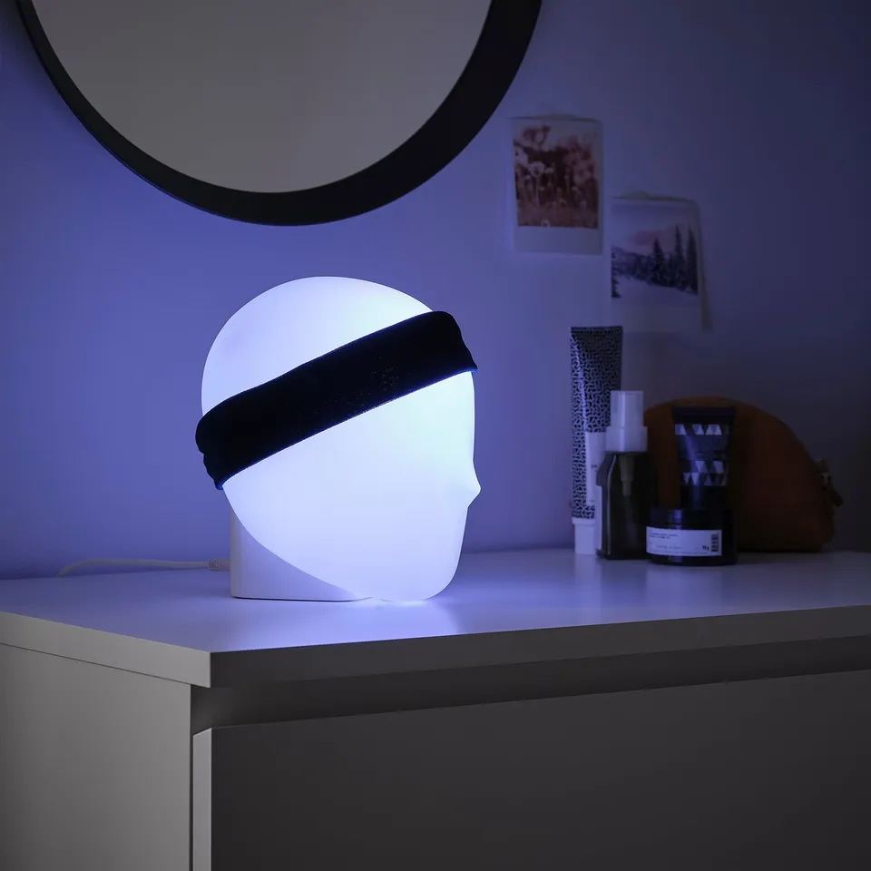 ISKÄRNA lamp in white, modern design with headband, sits on corpse-shaped base.