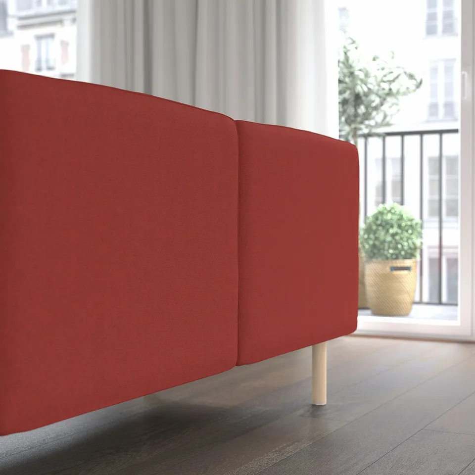 Red modular sofa near a large window. The sofa has a sleek design and is supported by wooden legs. The scene suggests a modern, well-lit room.