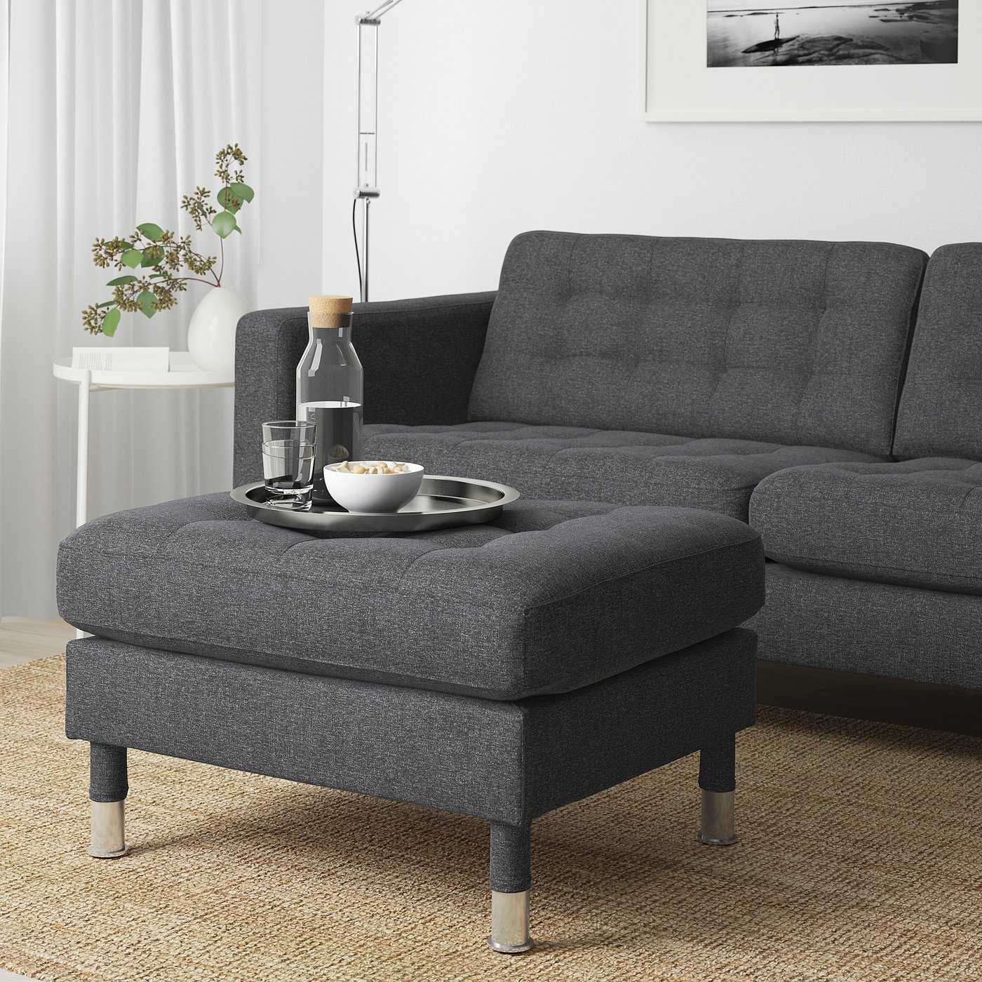 Modern living room with LANDSKRONA footstool, sofa, and vase of dried flowers. Black and white artwork on wall.