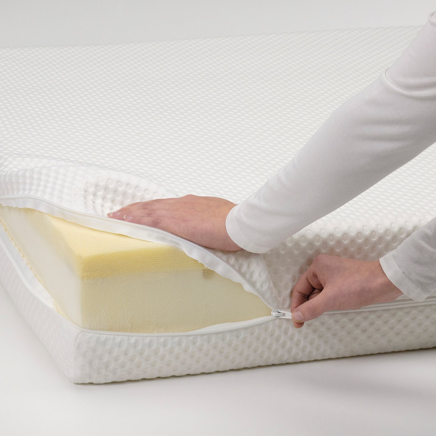 Person zips mattress protector onto firm foam mattress.