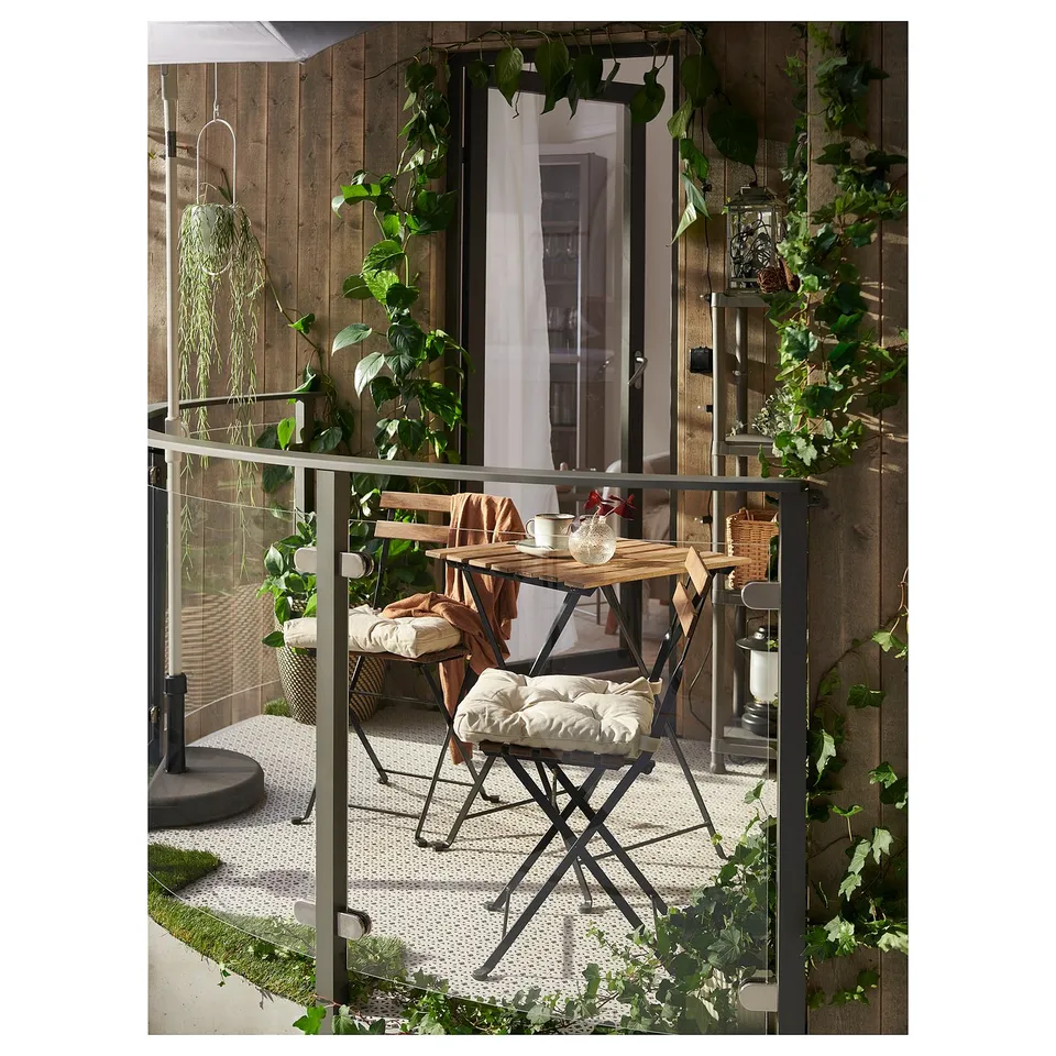 Cosy balcony setup with TÄRNÖ table & chairs, cushions, plants, and lanterns.