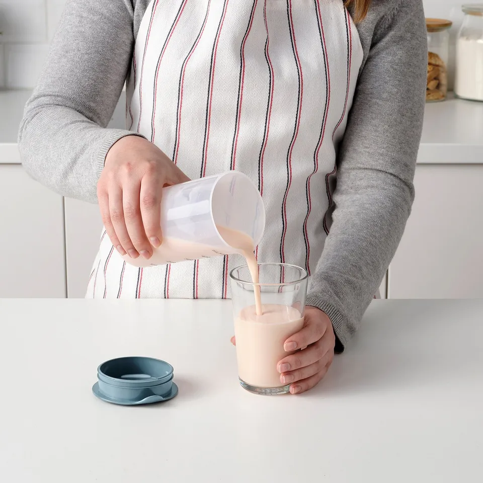 Person pours liquid from a measuring shaker into a glass on a kitchen counter.