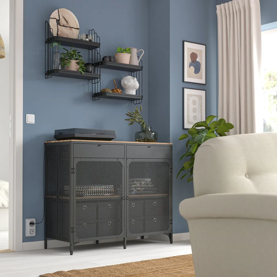 Black metal wall shelf with 3 tiers, plants, wood slice; blue wall, white chair.