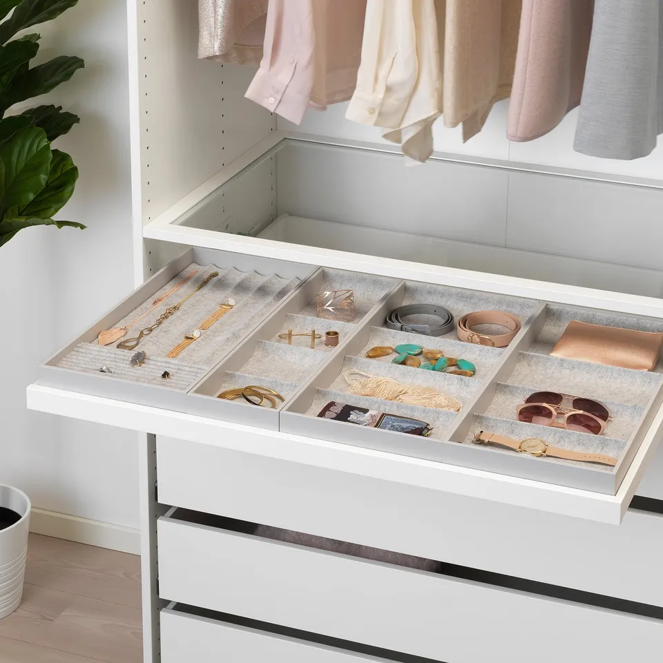 White wardrobe drawer with grey felt jewellery organiser, displaying necklaces, rings, and watches.