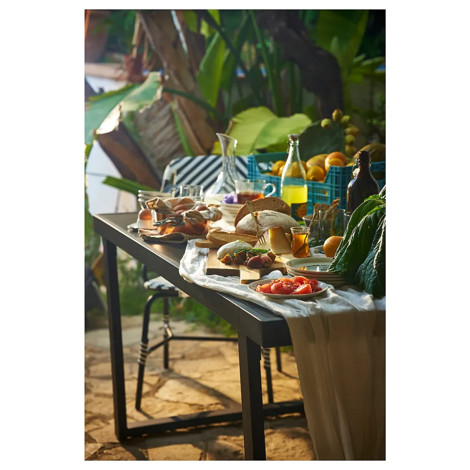 Outdoor dining set with modern table, black chairs, food, and plants.