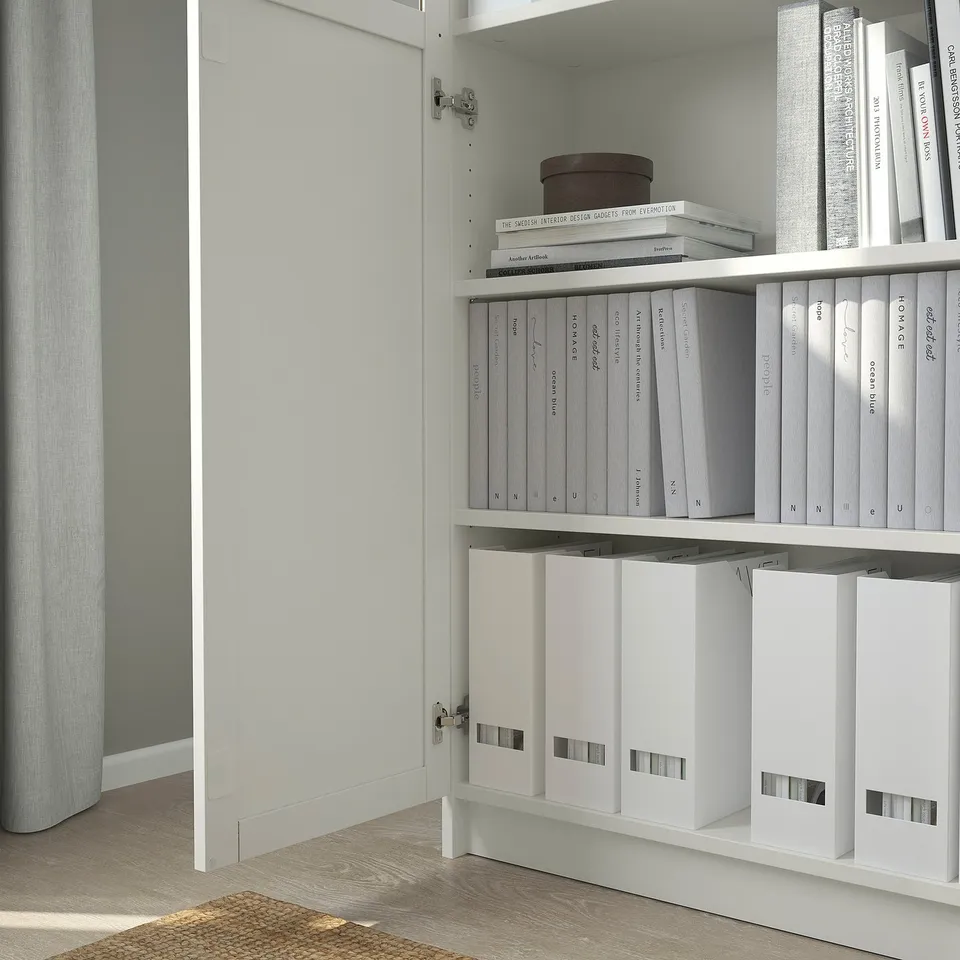 White BILLY bookcase with adjustable shelves, neatly organising grey and white books and white boxes.