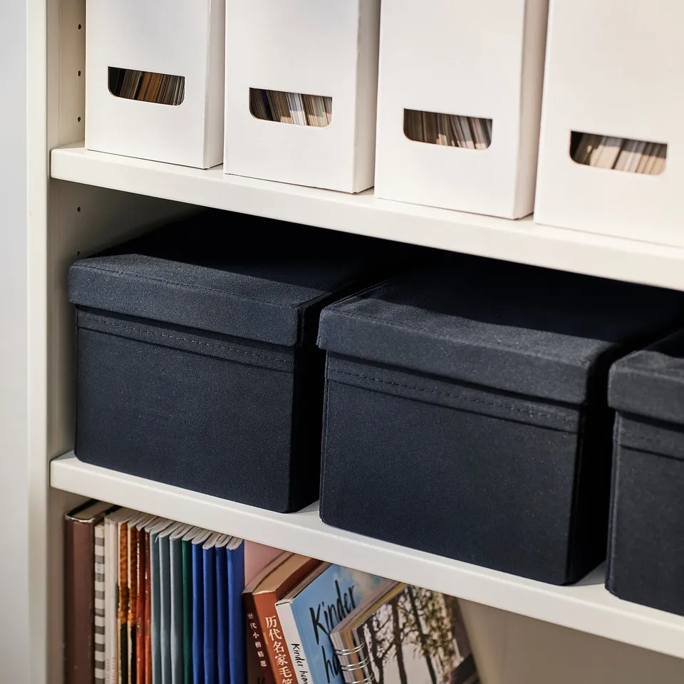 Shelf with black fabric boxes and white boxes, labelled DRÖNA. Fabric boxes have handles for easy access.