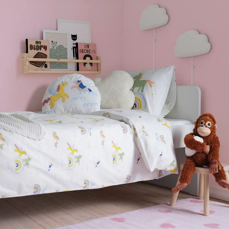 White unicorn & rainbow kids bed with organic cotton, cloud pillows, plush monkey, bookshelf, pink walls, clouds.