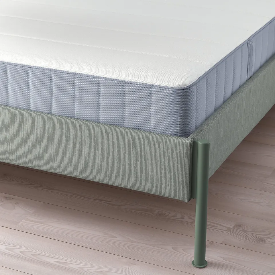 Close-up of TÄLLÅSEN bed frames corner, showcasing green metal legs and striped grey-green upholstery on bed sides.