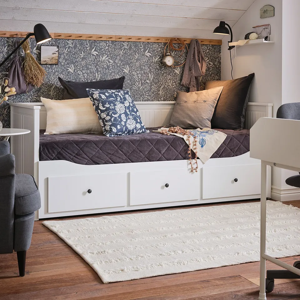 Cosy bedroom with white bed against patterned wall, SKURUP black lamps, grey pillows, and area rug.