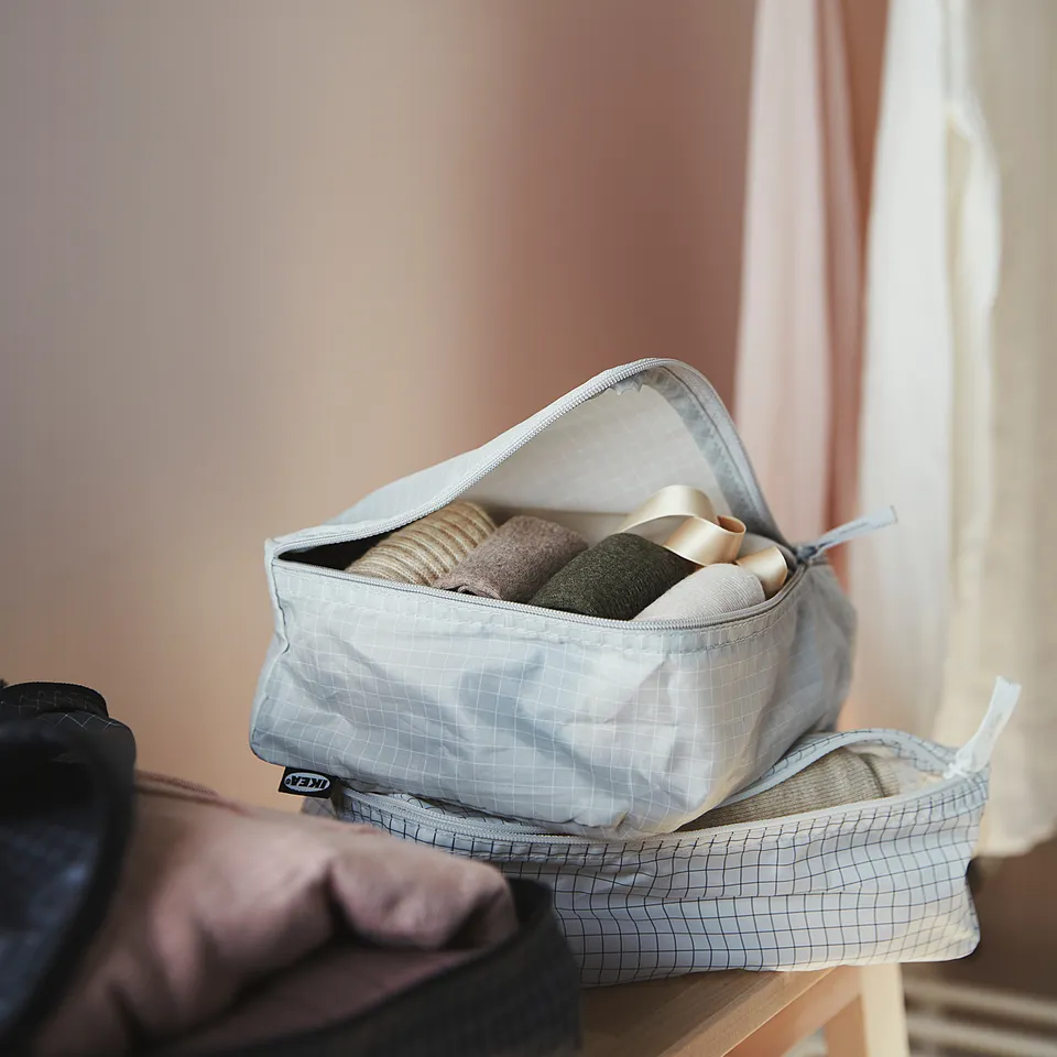 Image RENSARE storage bags, white with grey trim, holding rolled clothes on wooden shelf, with hangers and wall decor in background.